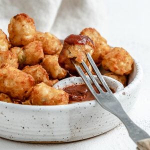 completed Air Fryer Tater Tots in a white speckled bowl with a fork in one being dipped in ketchup against a white background