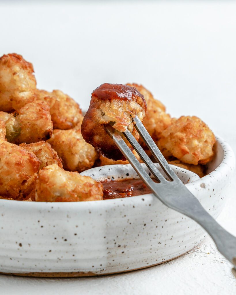 completed Air Fryer Tater Tots in a white speckled bowl with a fork in one tot against a white background