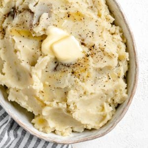 completed instant pot garlic mashed potatoes in a baking dish against a white background with a gray stripped towel in the background