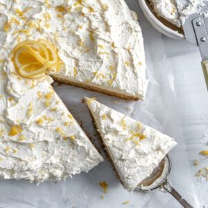 completed lemon cake with one piece sliced slightly away from cake on a white surface