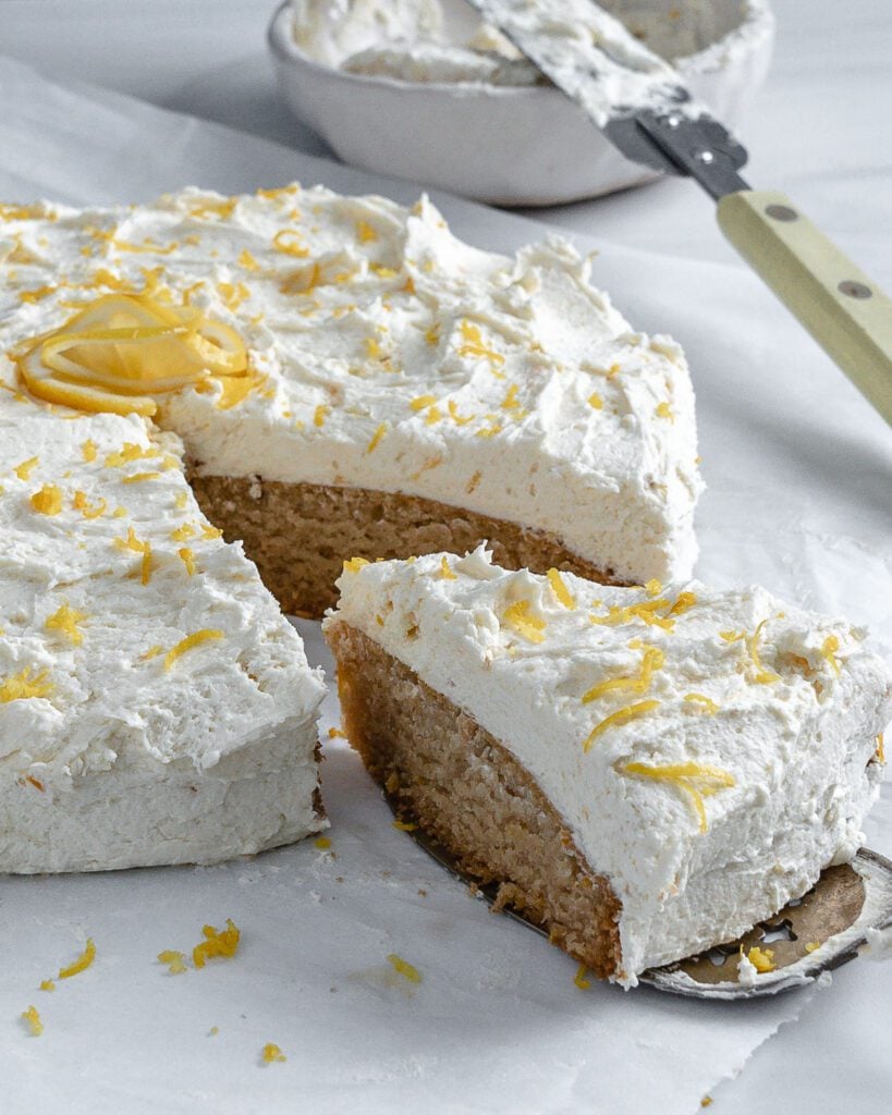 completed lemon cake with one piece sliced slightly away from cake on a white surface