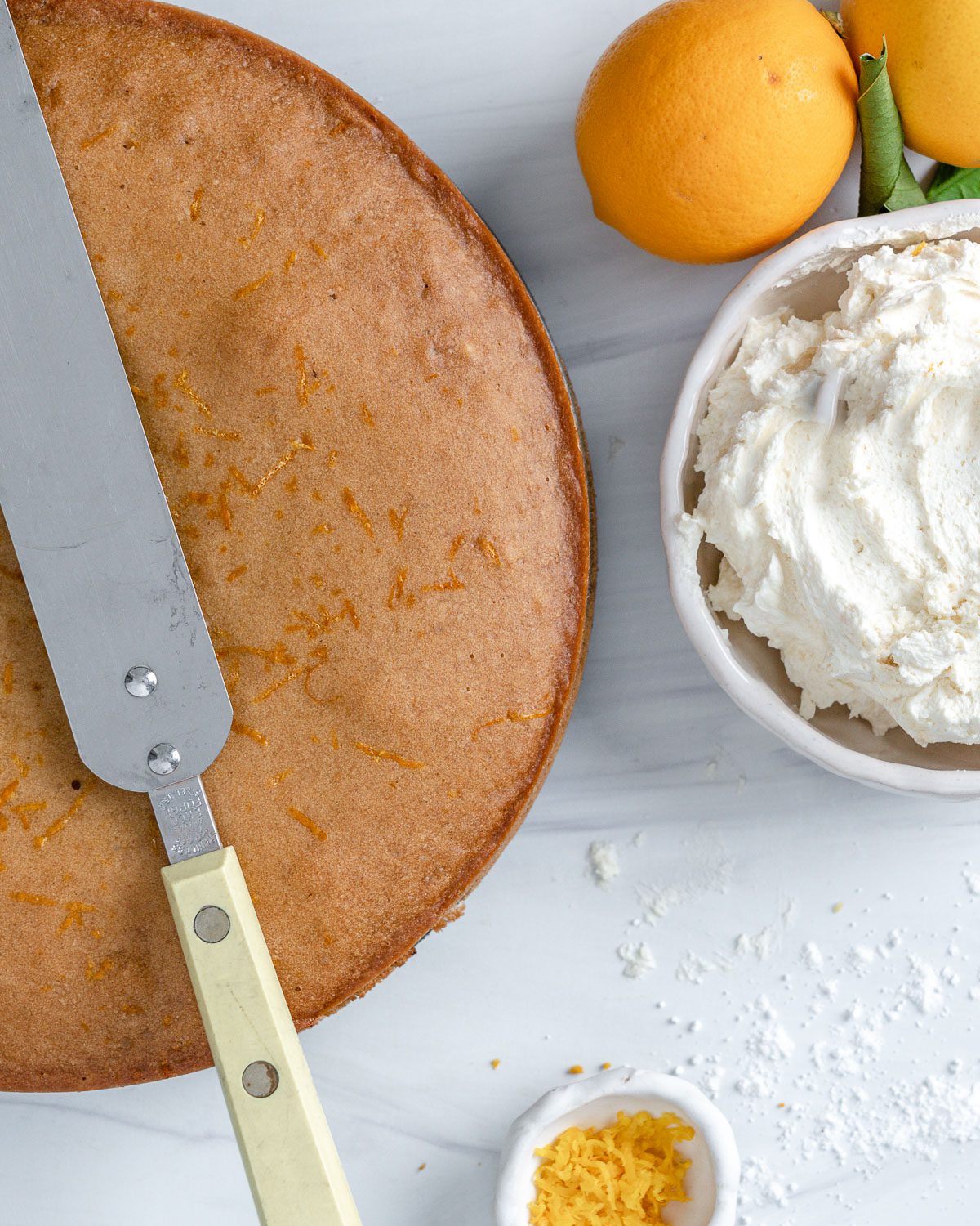 completed lemon cake pre frosting with ingredients in individual bowls against a white background