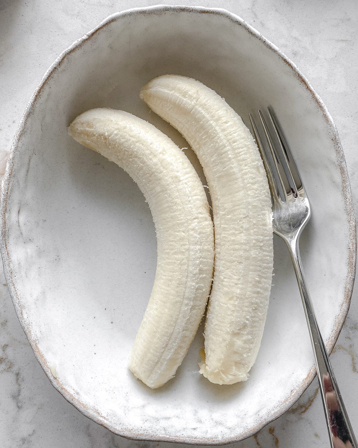 two peeled bananas in a white bowl with a fork