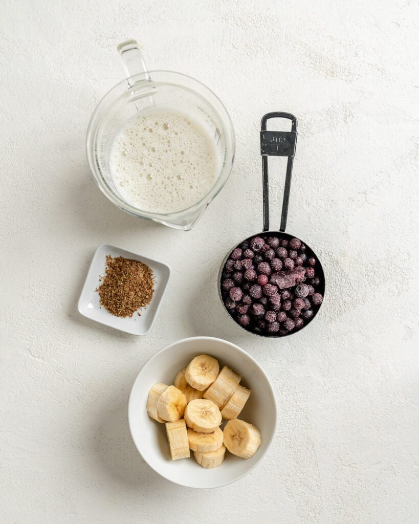 ingredients for blueberry banana smoothie measured out in bowls against a white background