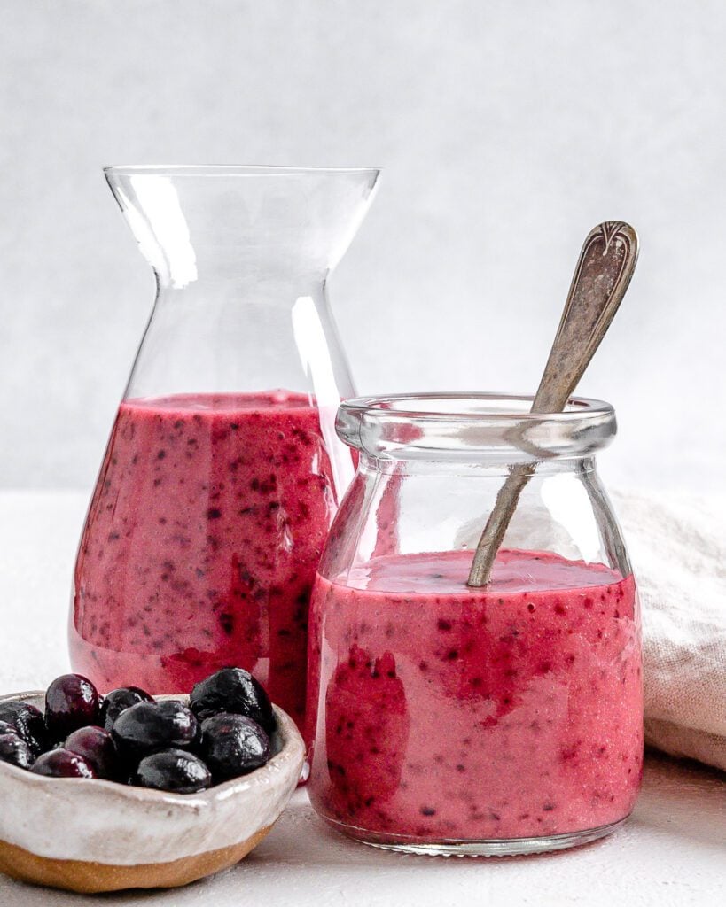 completed Blueberry Vinaigrette in two glass jars against a white background with blueberries in a small bowl