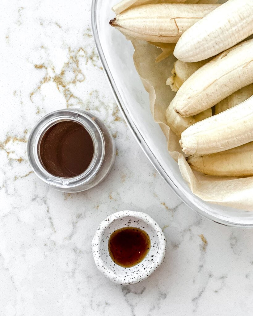 ingredients for Coffee Banana Nice Cream measured out in two serving bowls and a bowl of bananas against a white marble background