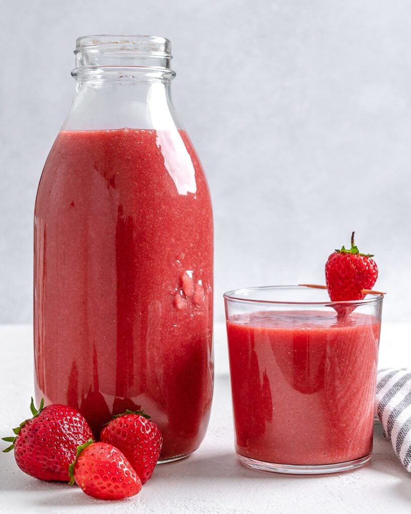 completed jar of strawberry juice and a cup of strawberry juice against a white background