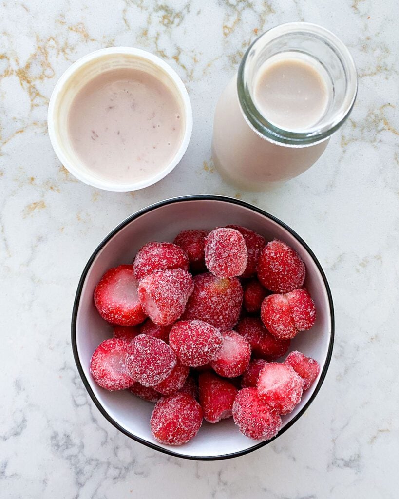 ingredients for strawberry yogurt smoothie measured out in individual bowls against a white background