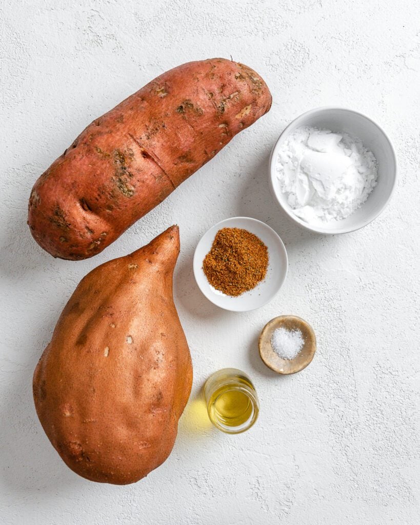 two whole sweet potatoes with ingredients measured out against a white background