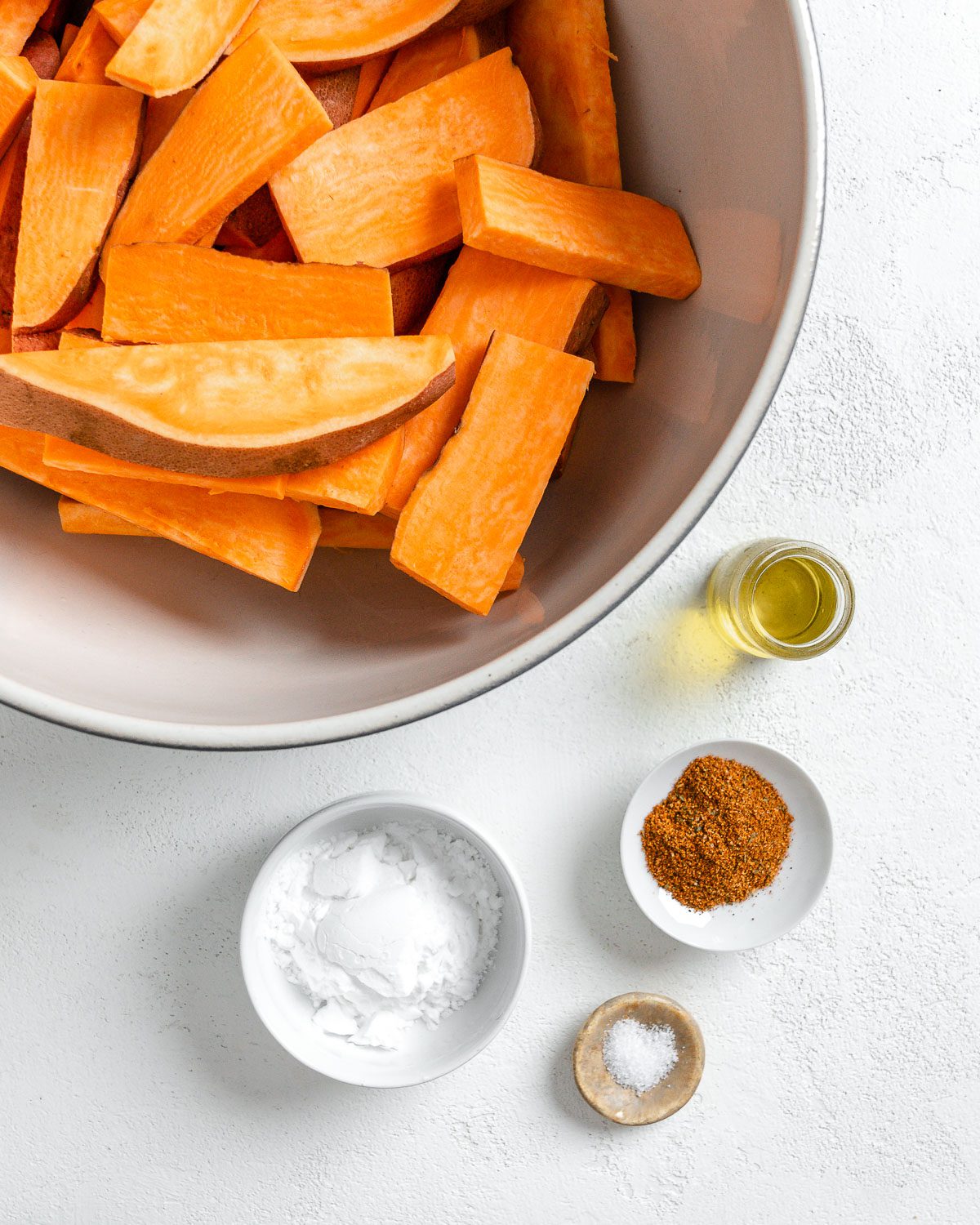 ingredients for sweet potato wedges measured out in individual bowls against a white surface