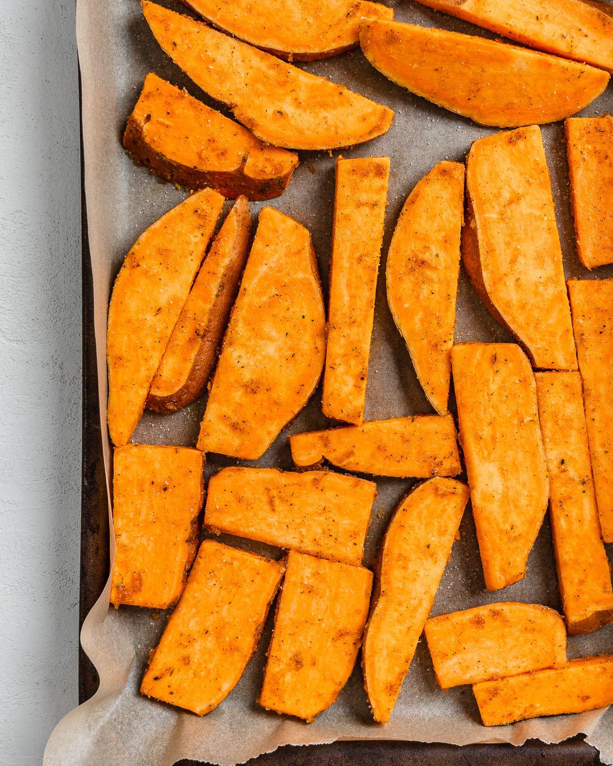 raw potato wedges on a baking tray against a white background