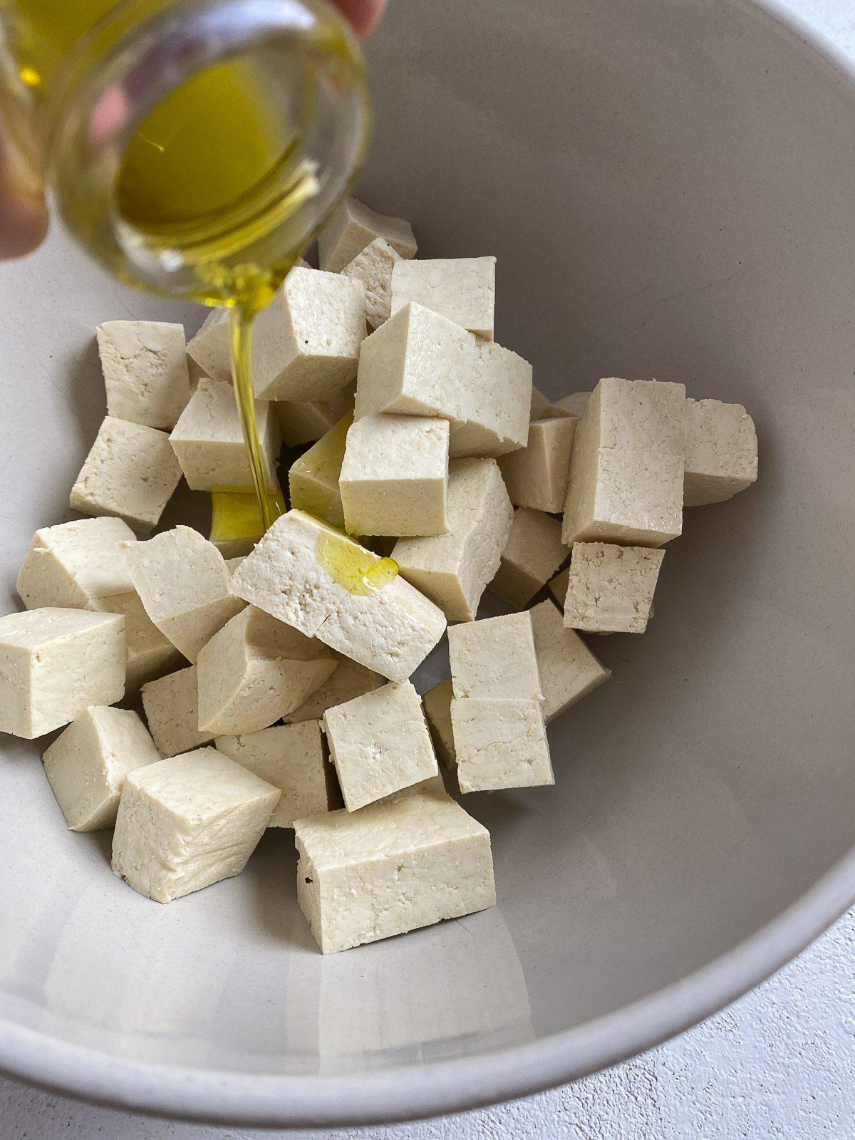 process shot of adding oil to cubed tofu in a white bowl