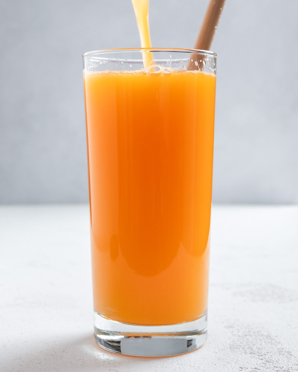 completed Apple OJ Carrot Juice in a glass against a white surface and light background