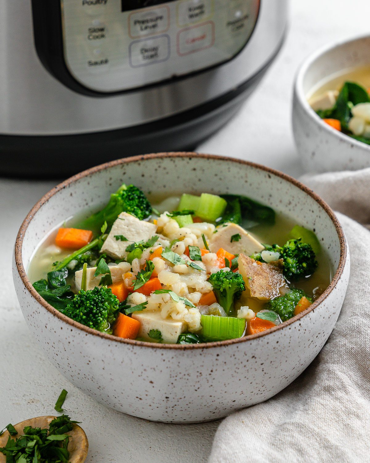 completed Instant Pot Vegetable Barley Soup in a white bowl against a white background with a pressure cooker in the background