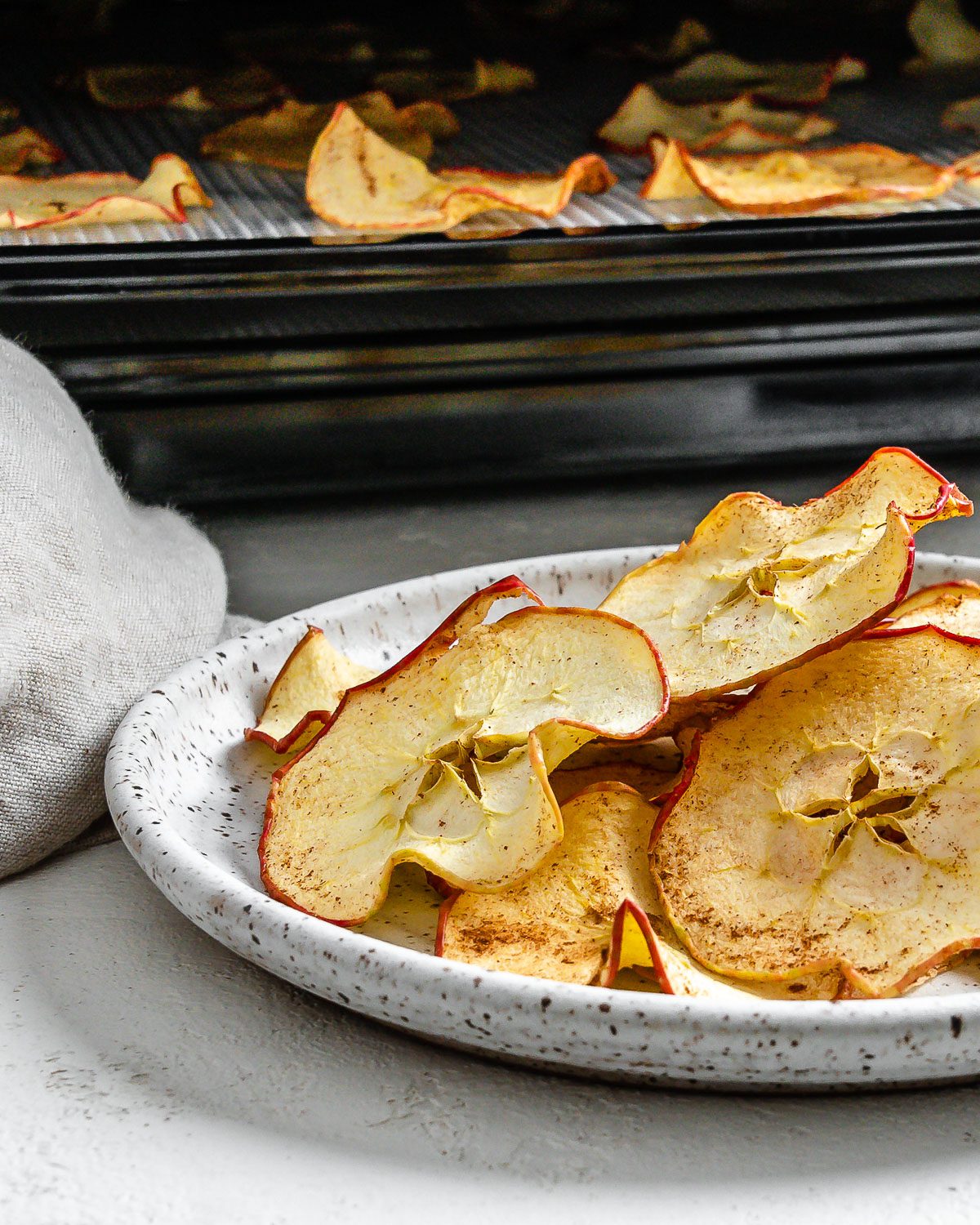 completed Dehydrator Apple Chips on a white plate with chips in the background