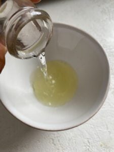 Water being poured into fresh lemon juice in a white bowl.