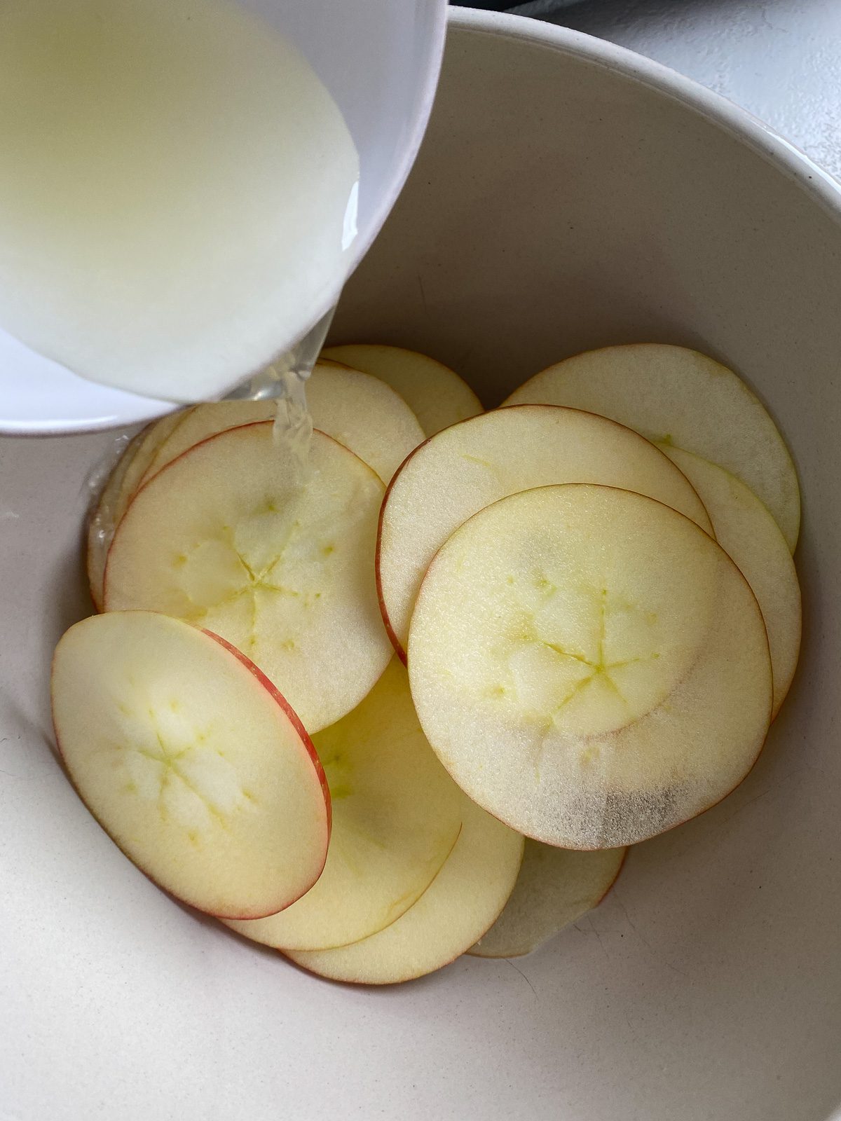process shot of adding lemon juice to sliced apples in white bowl