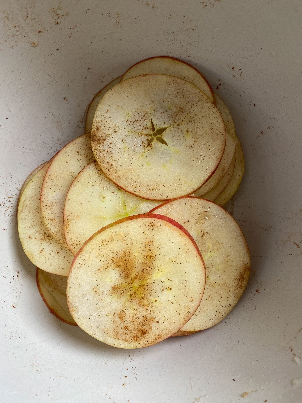 Thin apple slices tossed with lemon water and cinnamon in a white bowl.