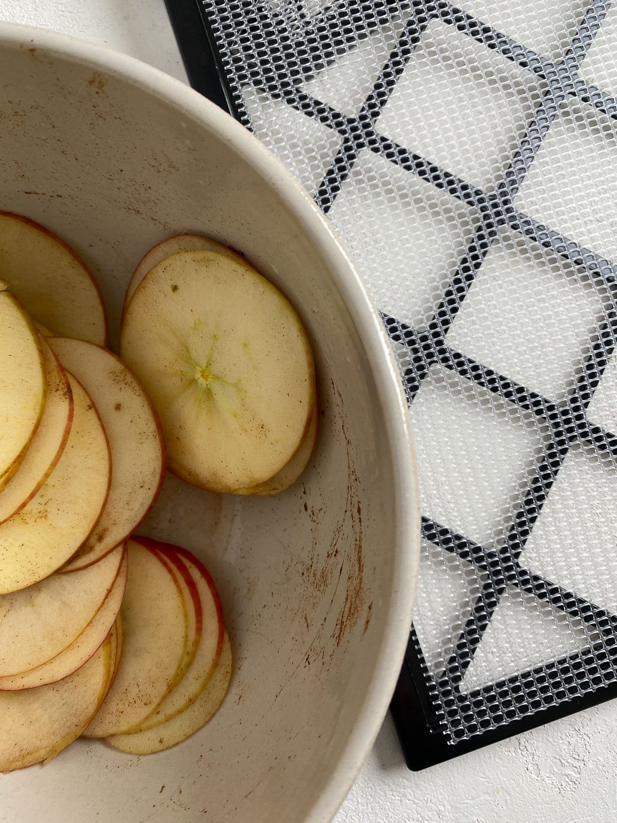sliced apples in bowl alongside dehydrator tray