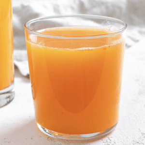 completed Apple OJ Carrot Juice in a glass against a white surface and light background