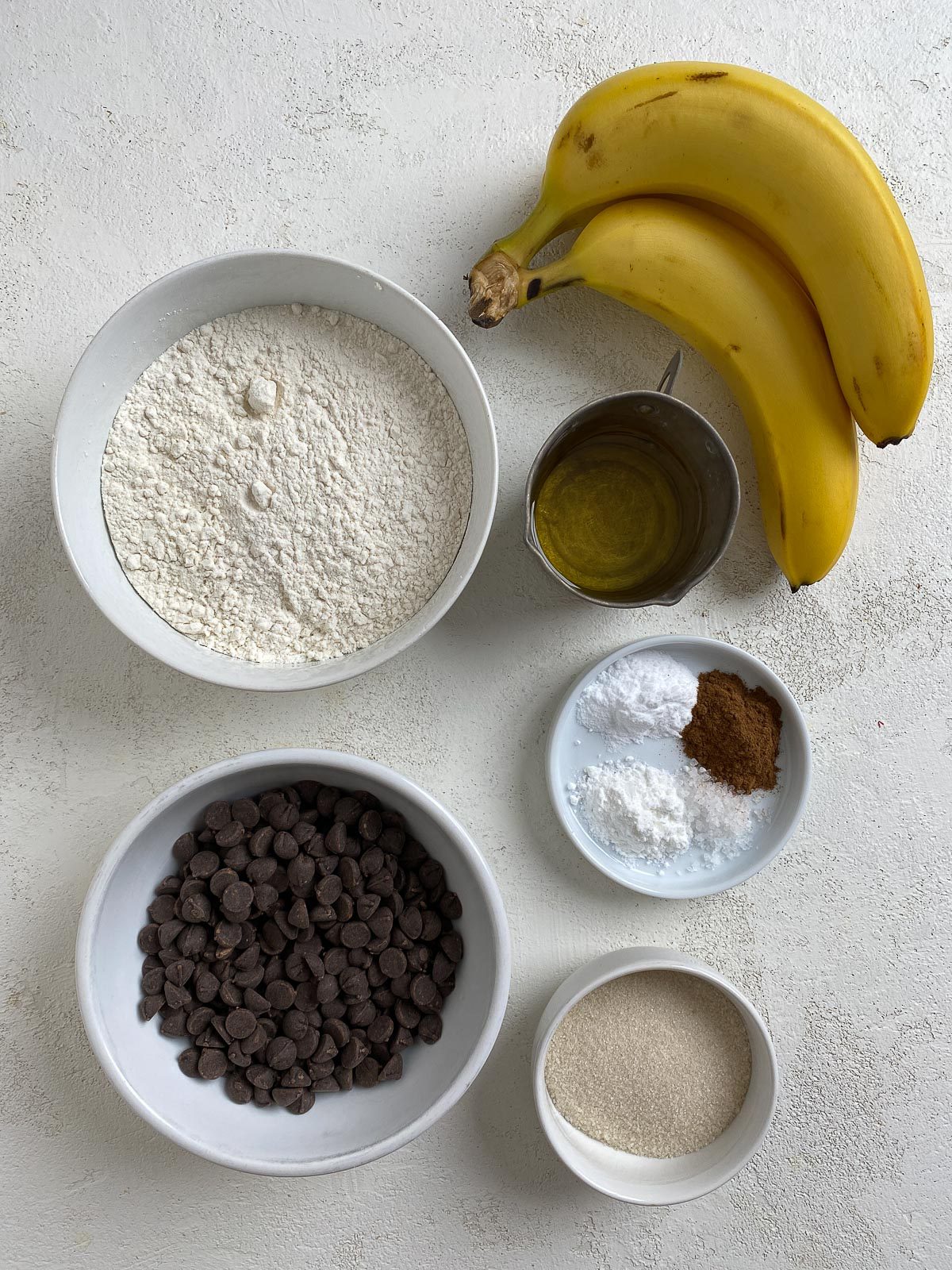ingredients for Vegan Chocolate Chip Banana Muffins measured out in small white bowls