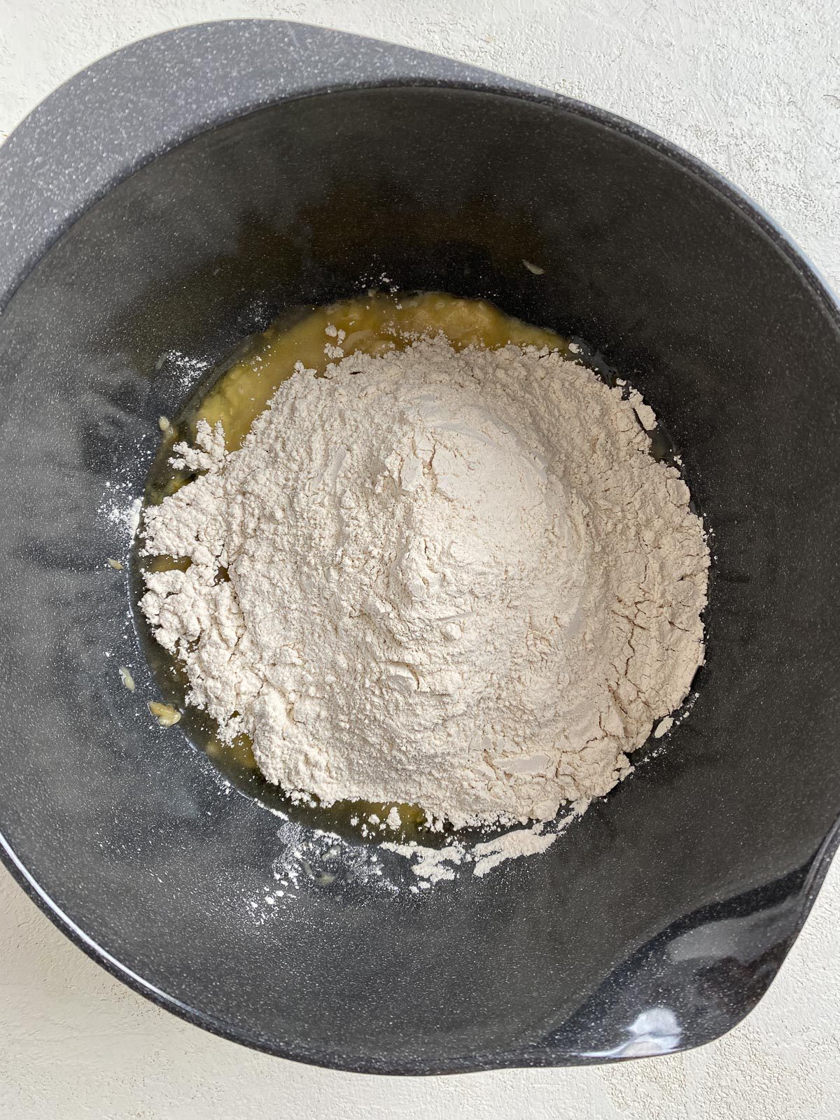 process shot of flour addition to bowl of mashed bananas