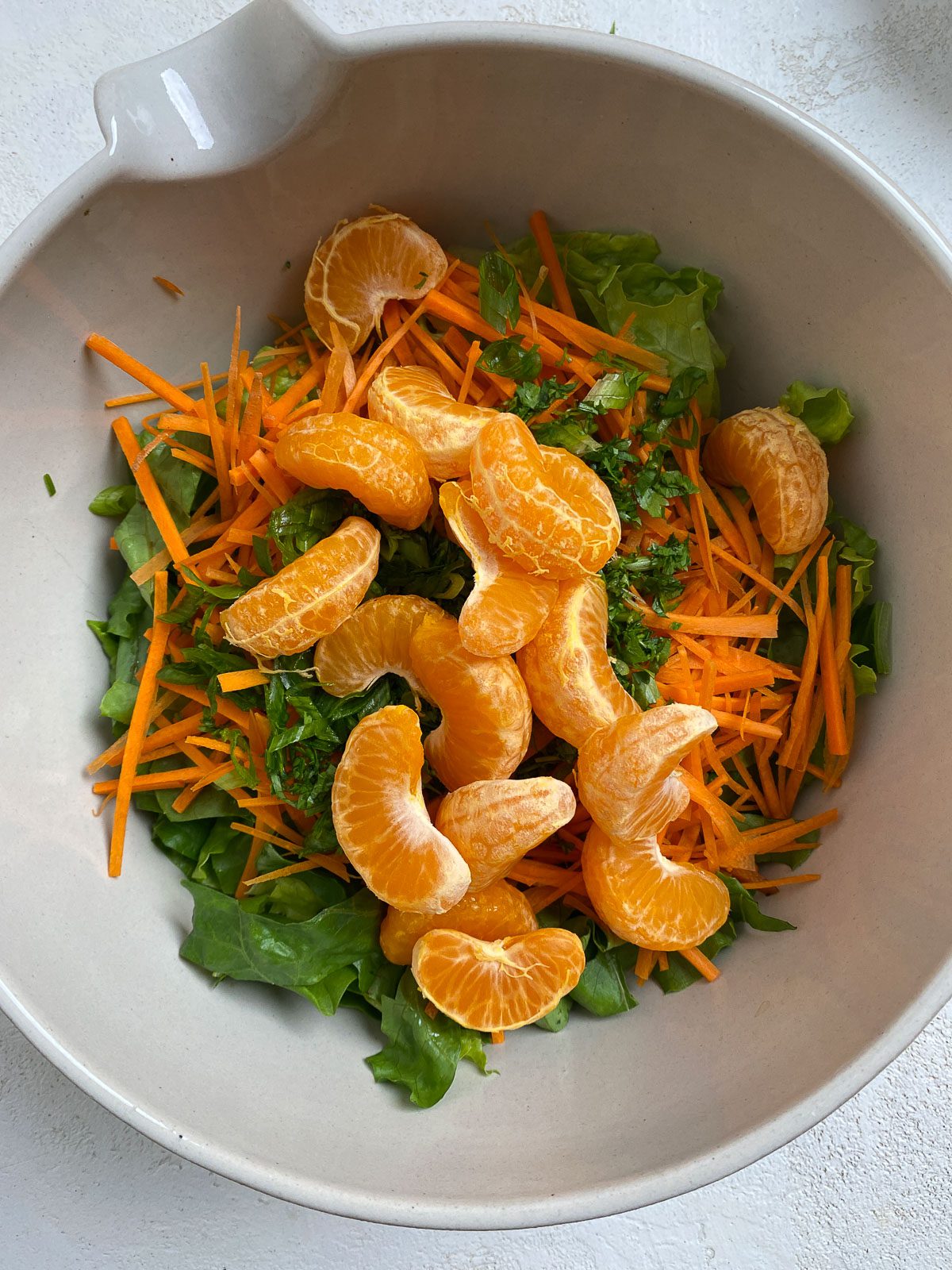 process of mandarin and carrots added to lettuce in white bowl