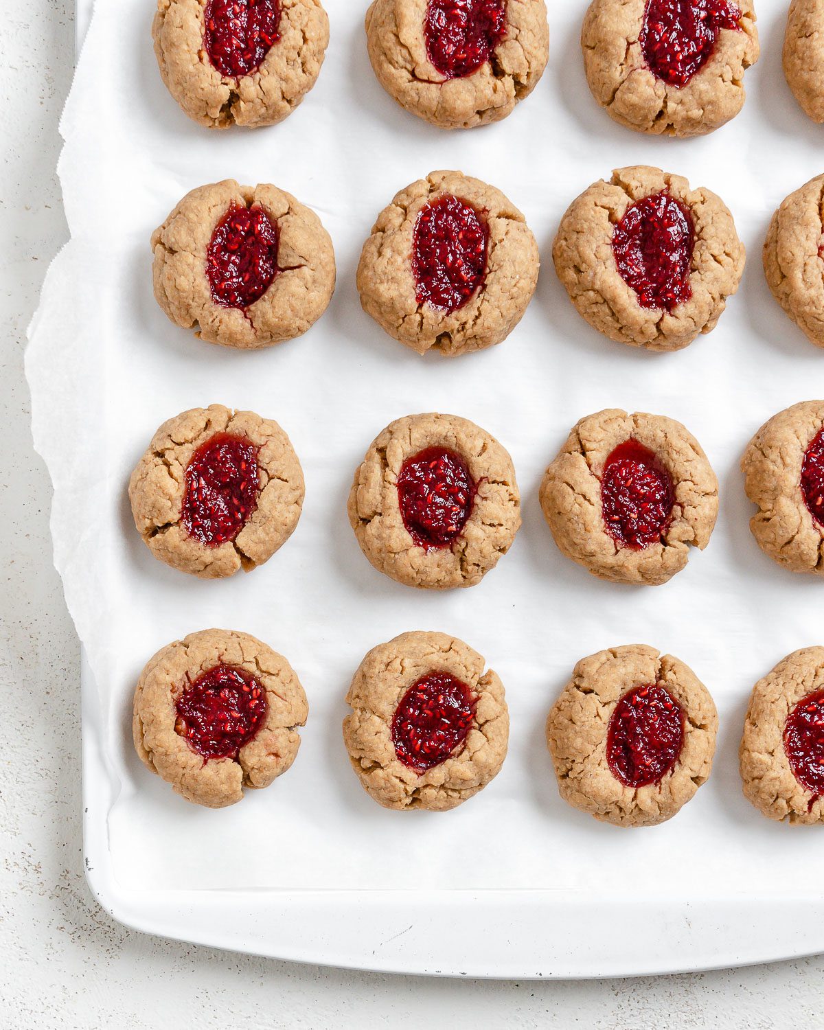 completed Vegan Peanut Butter and Jelly Thumbprint Cookies scattered on cookie sheet