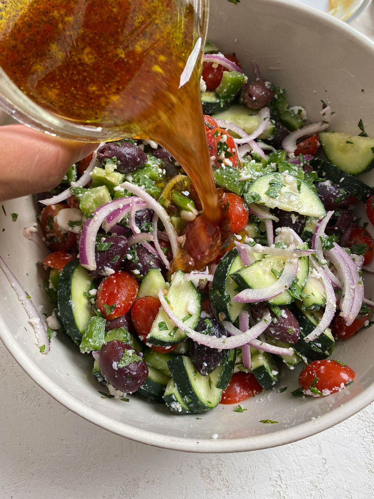 process shot showing the pouring of dressing onto bowl of vegan greek salad