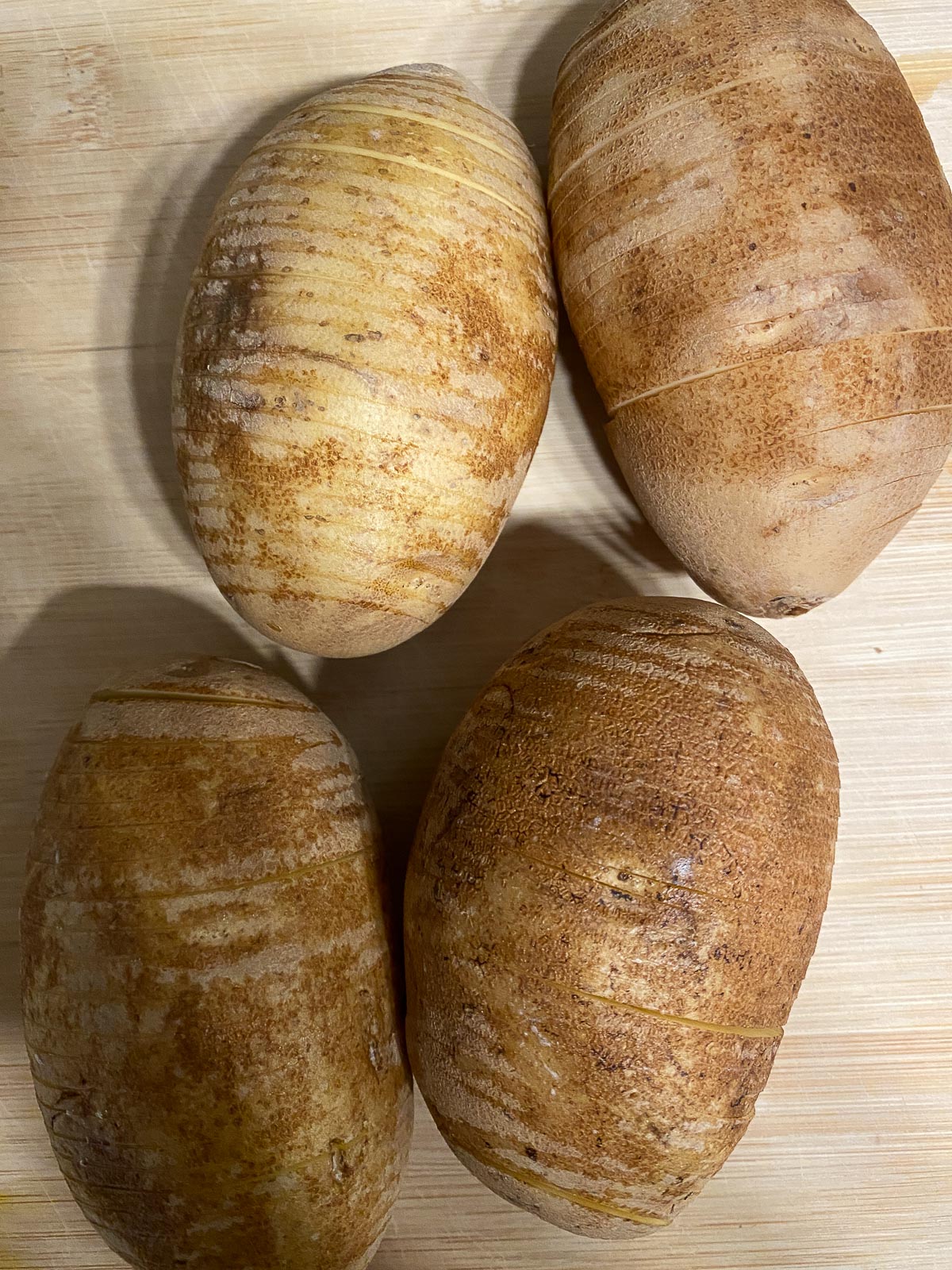 four cut potatoes in a hassleback format against a cutting board