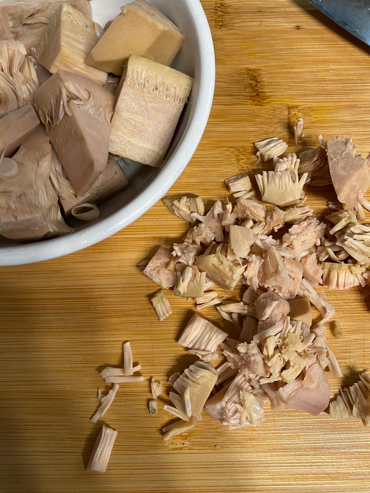 shredded jackfruit alongside a bowl of jackfruit on a brown cutting board