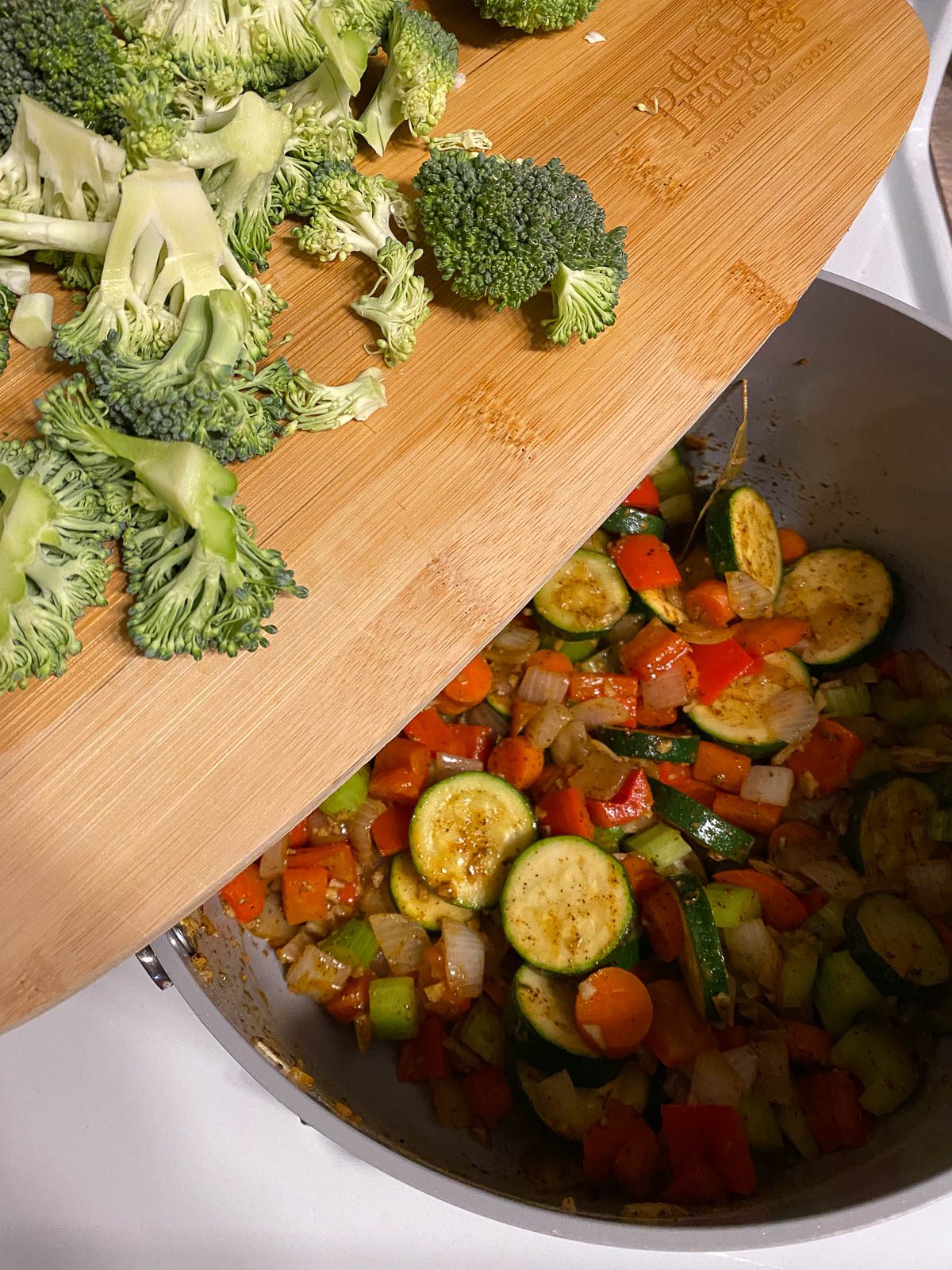 process of adding broccoli to mixed pan of veggies