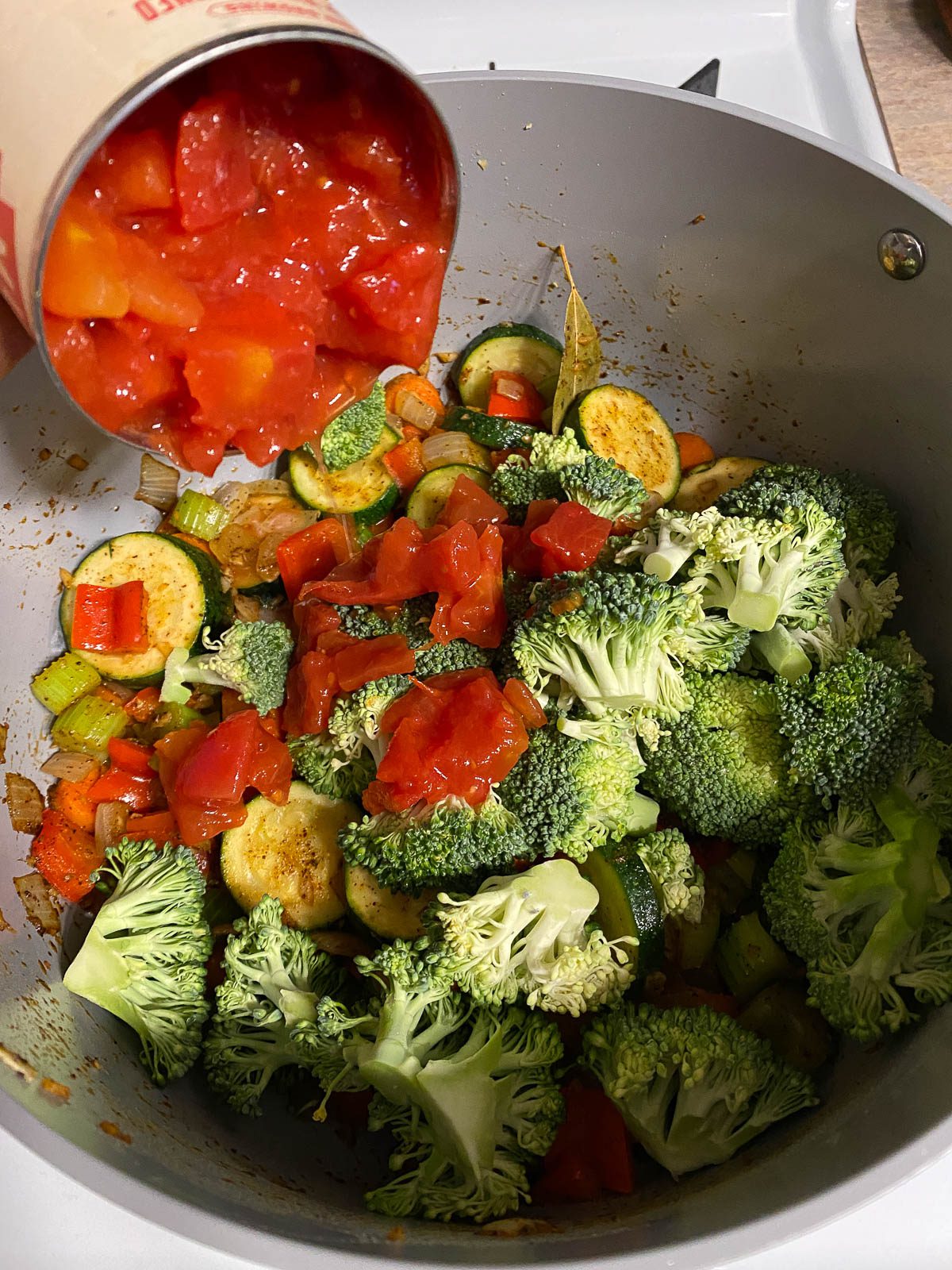 process of adding diced tomatoes to mixed pan of veggies