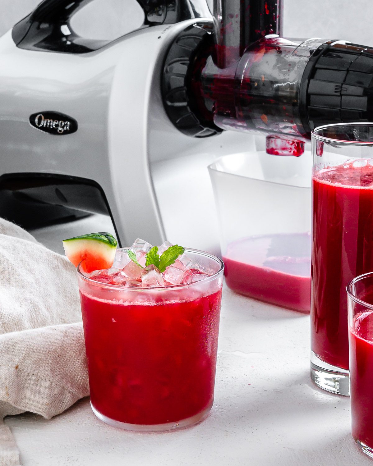 completed Fresh Watermelon Juice Blend in a glass cut with two cups and juicer in the background
