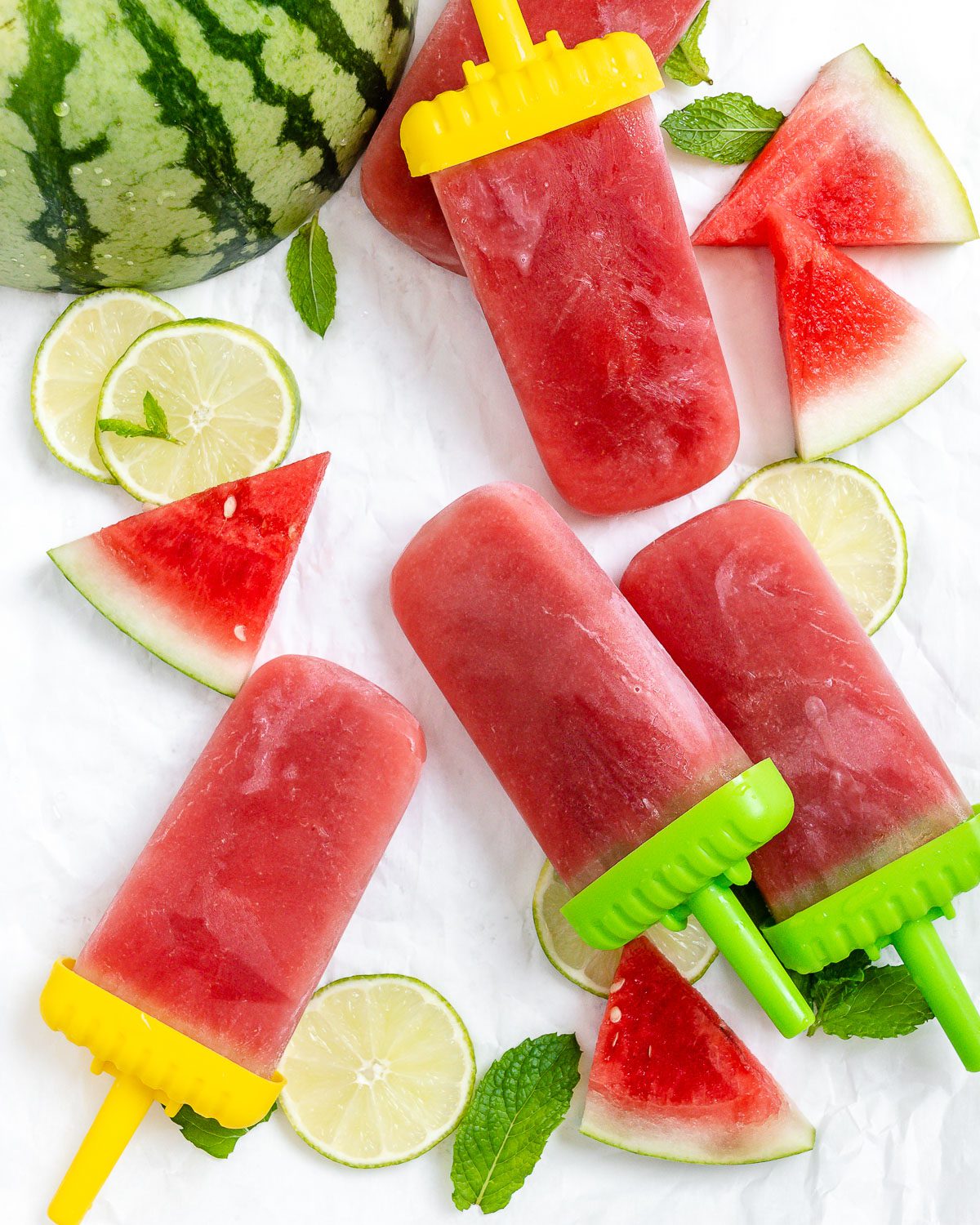 four completed Watermelon Popsicles with watermelon scattered in the background