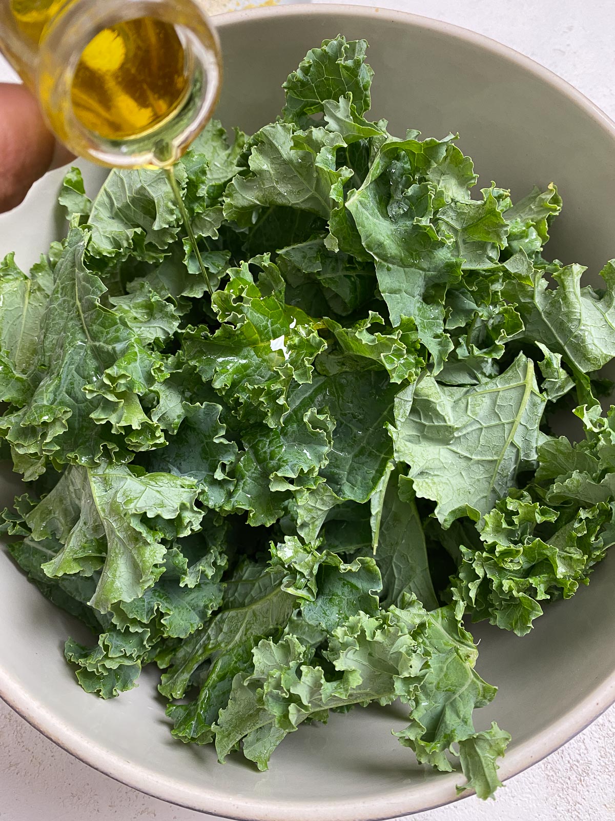 process of oil being added to kale in white bowl