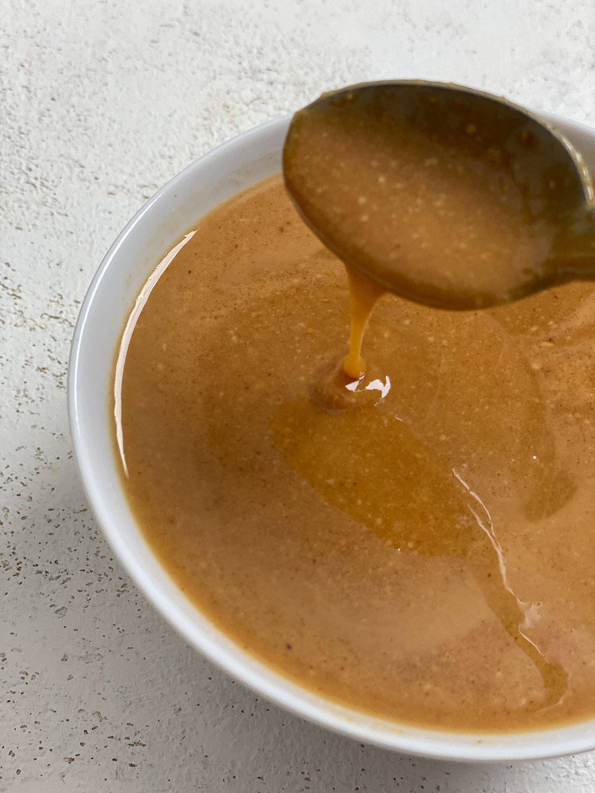 completed Simple Vegan Caramel in a bowl with caramel drizzling down from a spoon against a white background