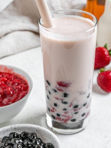completed Strawberry Boba Tea in a glass cup with ingredients in the background