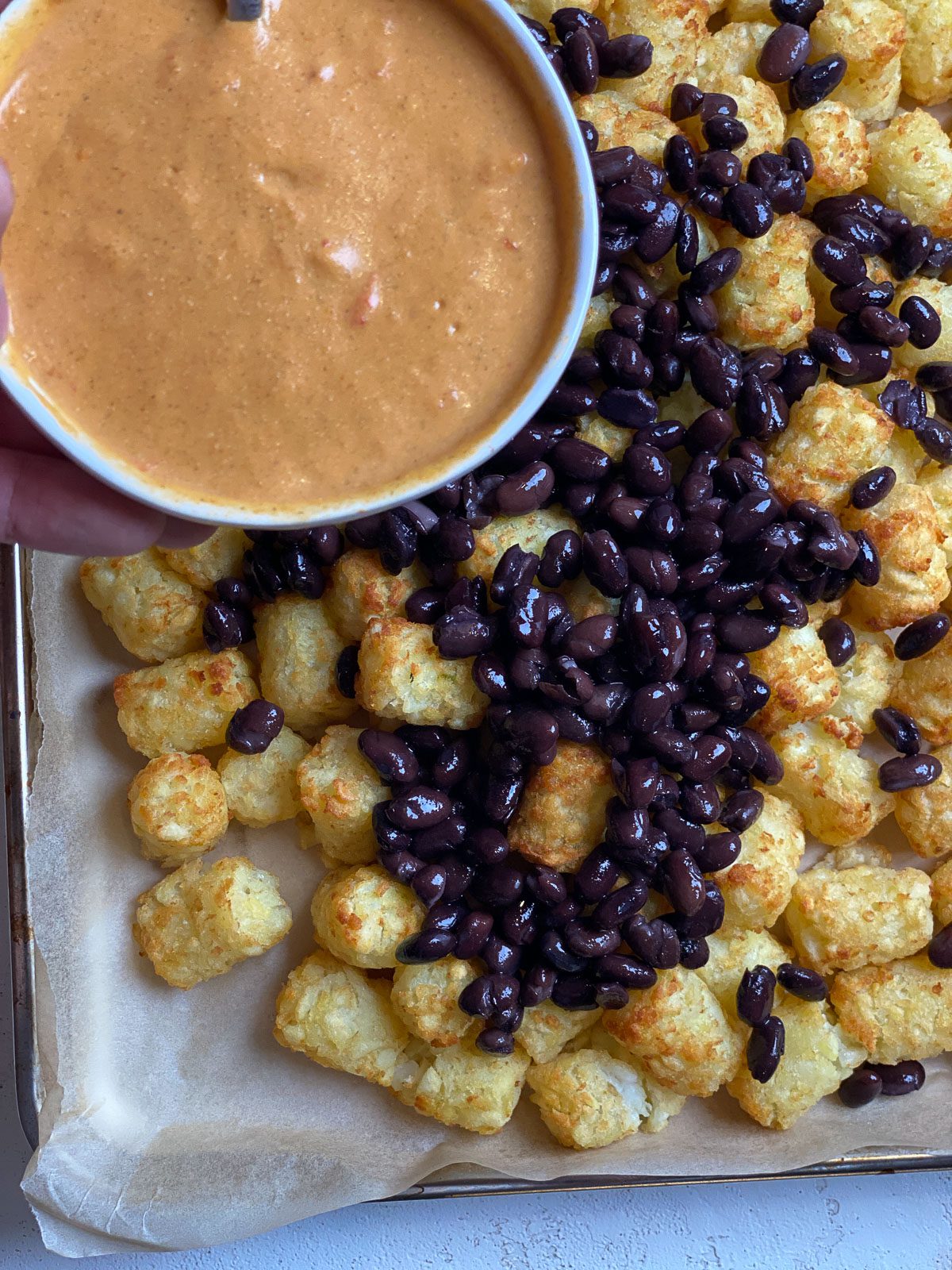 process of adding nacho sauce to tater tots and beans