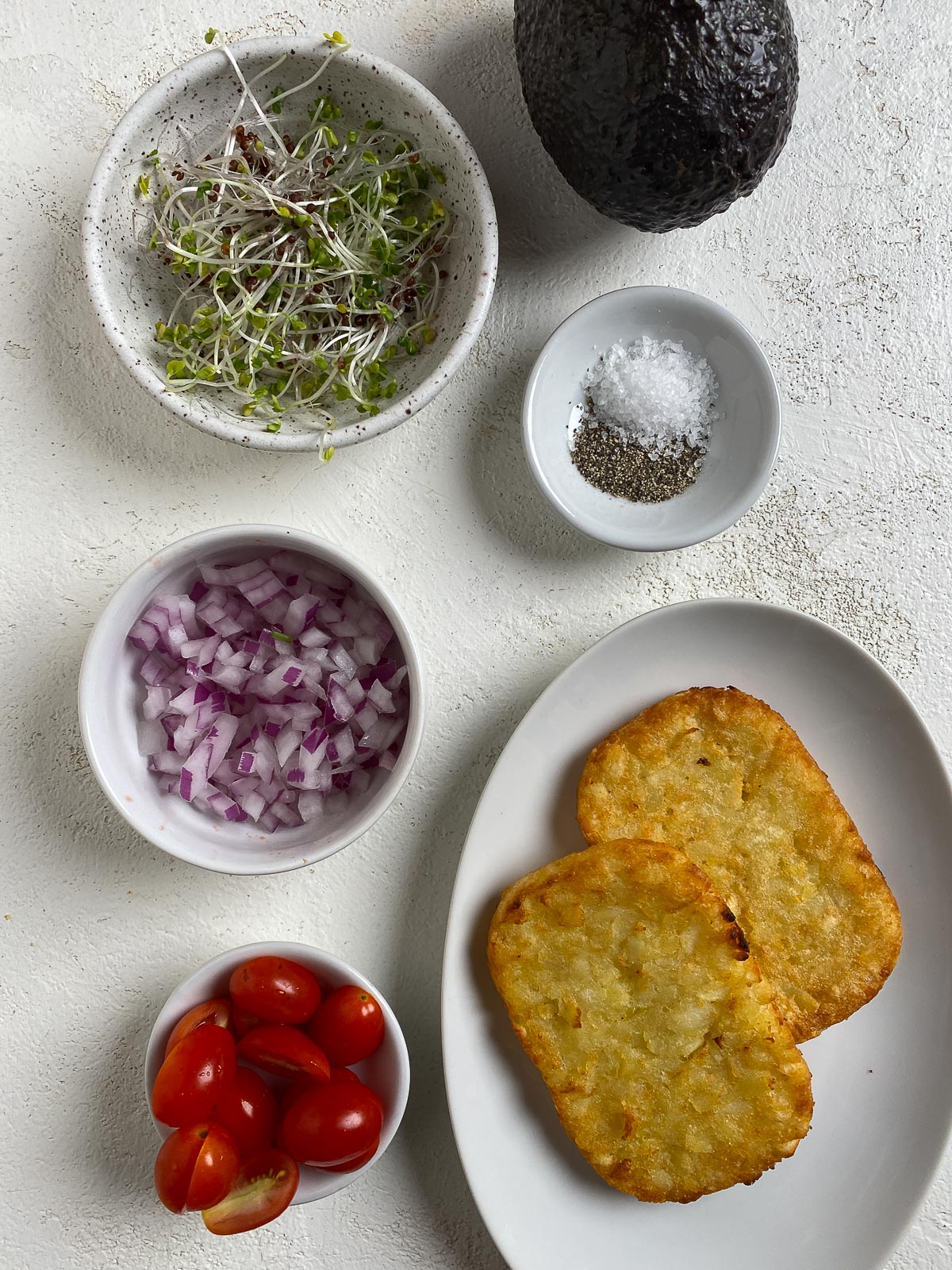ingredients for Smashed Avocado Hashbrown Toast measured out in individual platters against a light surface
