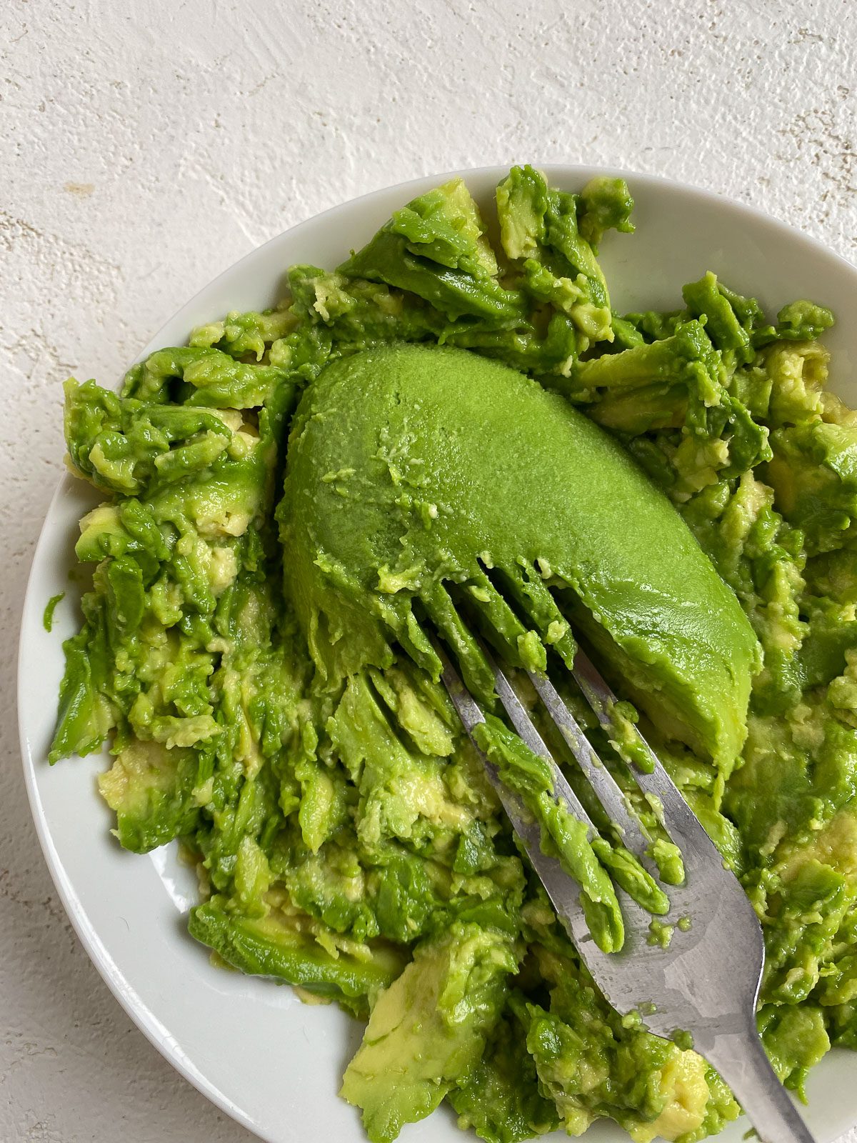 process shot of smashed avocado on a white plate