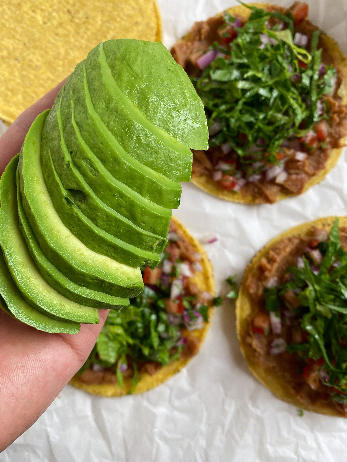 process of avocado slices being added to vegan bean tostada