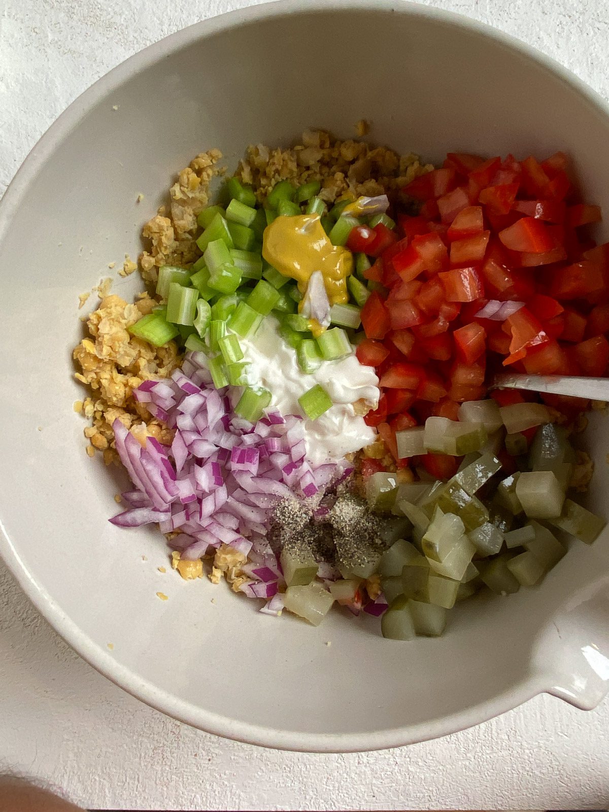 process of adding additional ingredients for a vegan chickpea salad sandwich in a white bowl