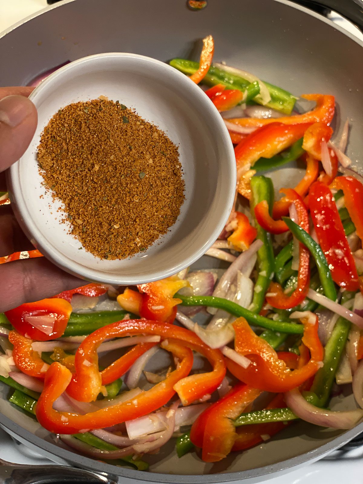 process of seasonings being poured into pan of veggies