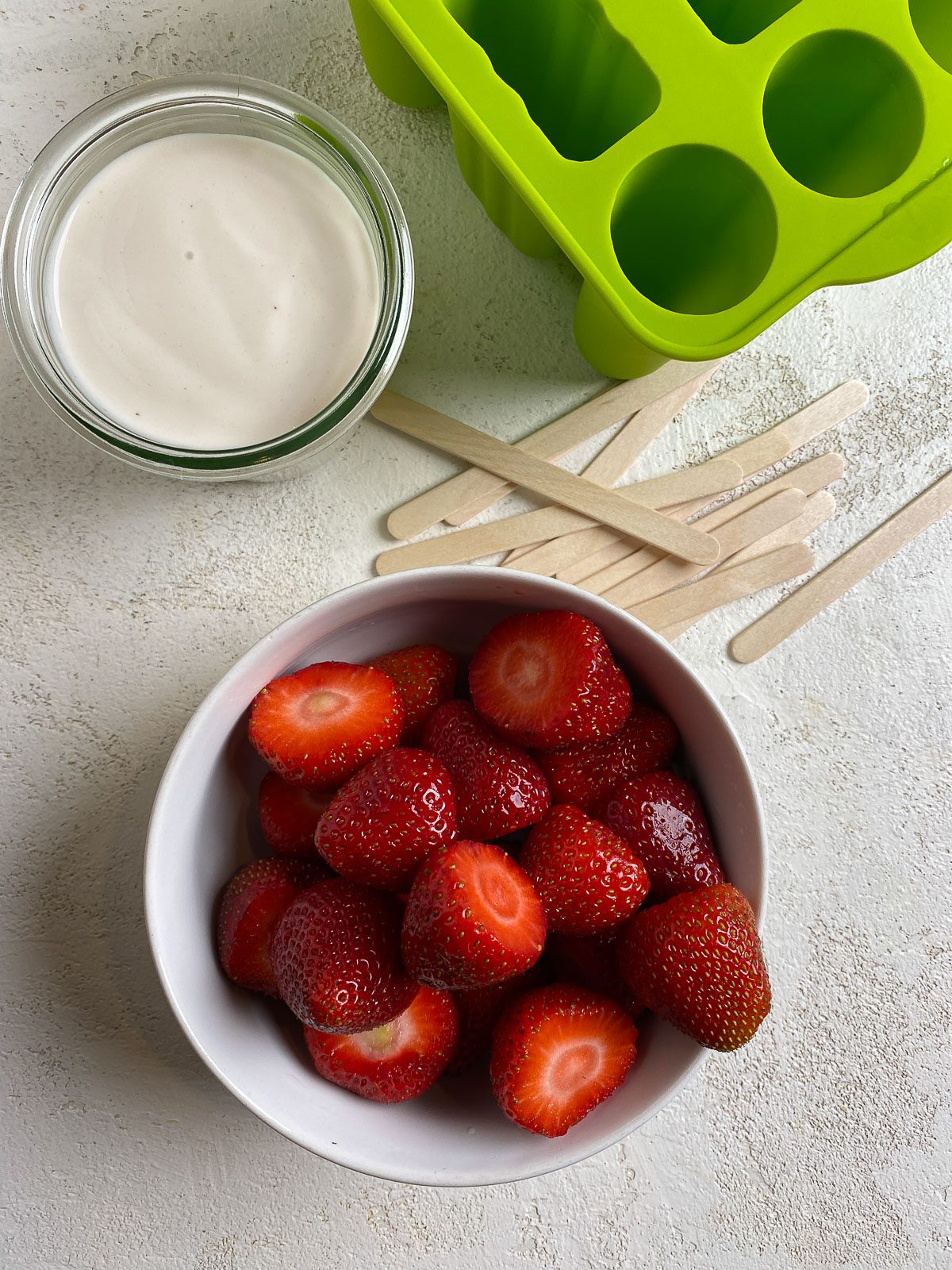 a bowl of strawberries alongside vegan yogurt and popsicles mold