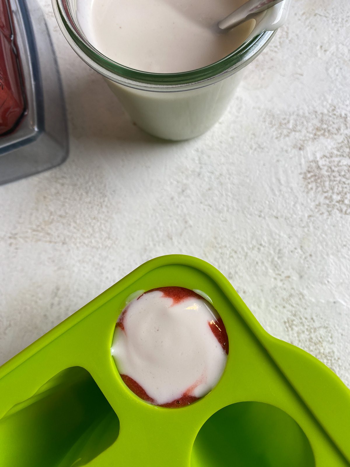 strawberry mixture and vegan yogurt in a popsicle mold against a white surface