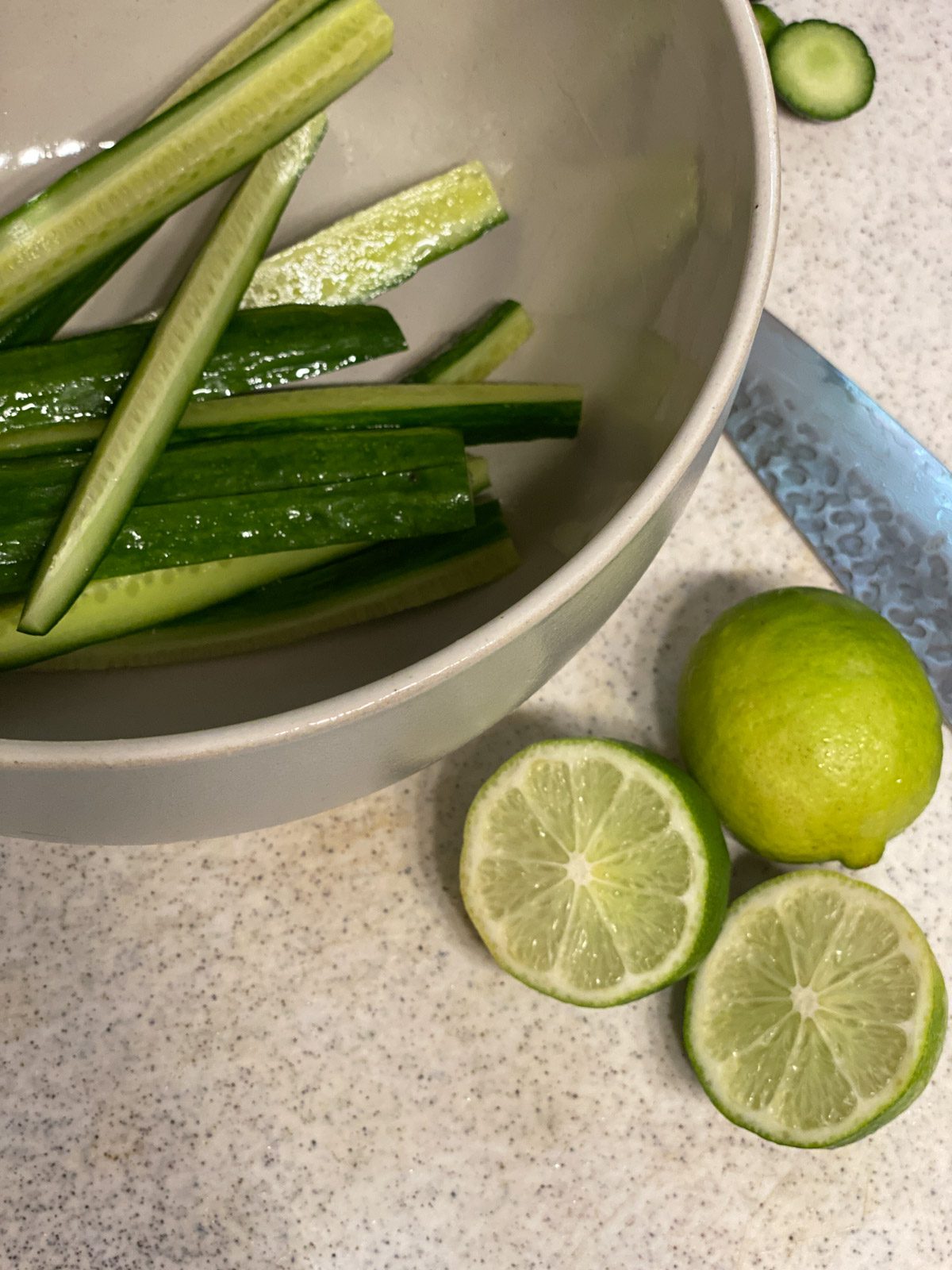 sliced cucumbers in a bowl alongside halves of lime
