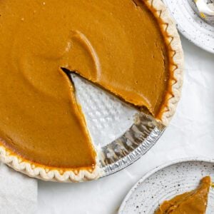 completed Easy Vegan Pumpkin Pie with a slice missing and plated on a separate plate against a white background
