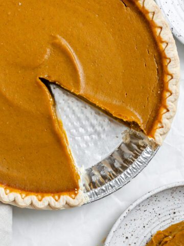 completed Easy Vegan Pumpkin Pie with a slice missing and plated on a separate plate against a white background