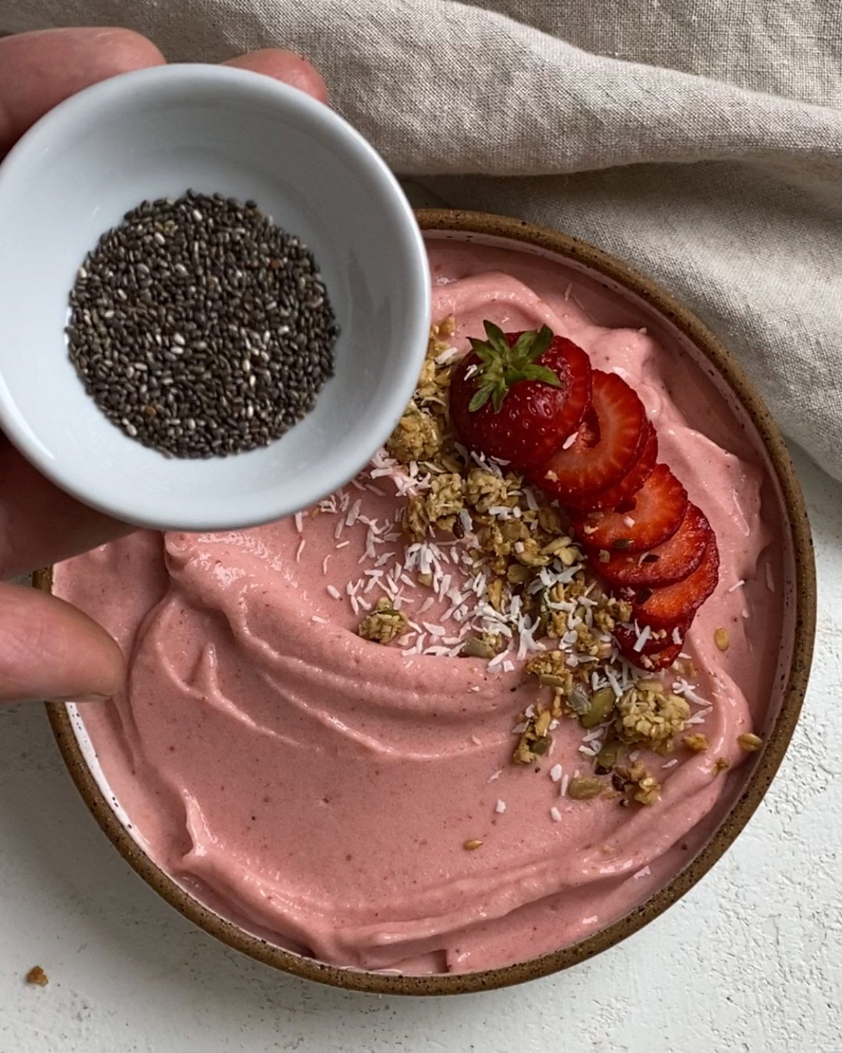 process of adding chia seeds to top the Strawberry Smoothie Bowl